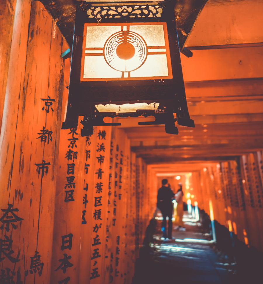 Linterna tradicional en Fushimi Inari, Kioto, entre torii naranjas al atardecer