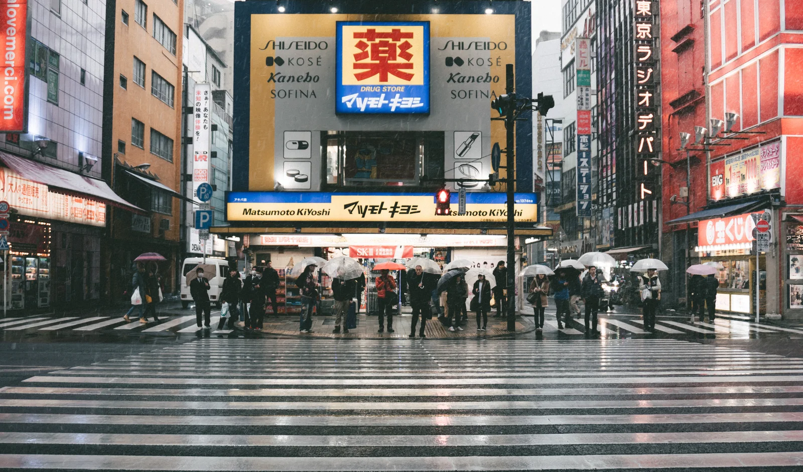Cruce de peatones en Tokio bajo la lluvia con paraguas y tiendas iluminadas