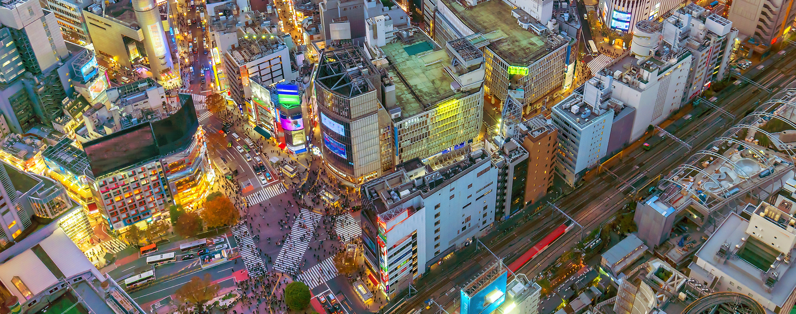 Vista aérea de Shibuya en Tokio con edificios iluminados, calles y cruce urbano al atardecer